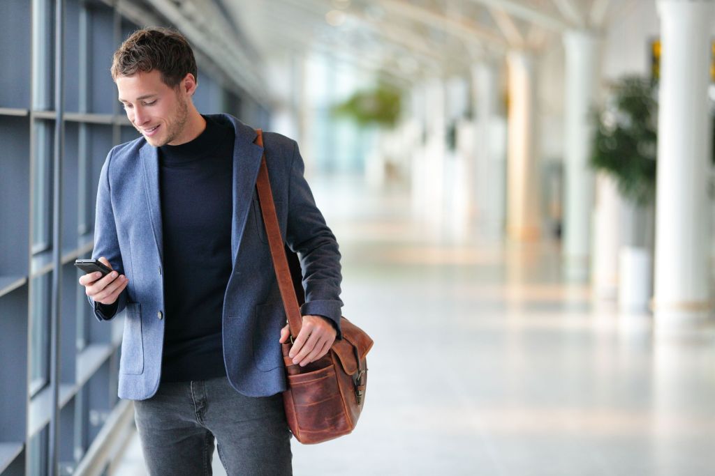 Culture-Videos-2go-65498953_m 65498953 - business man using mobile phone app in airport. young business professional man texting smartphone walking inside office building or airport terminal. handsome man wearing stylish suit jacket indoors.