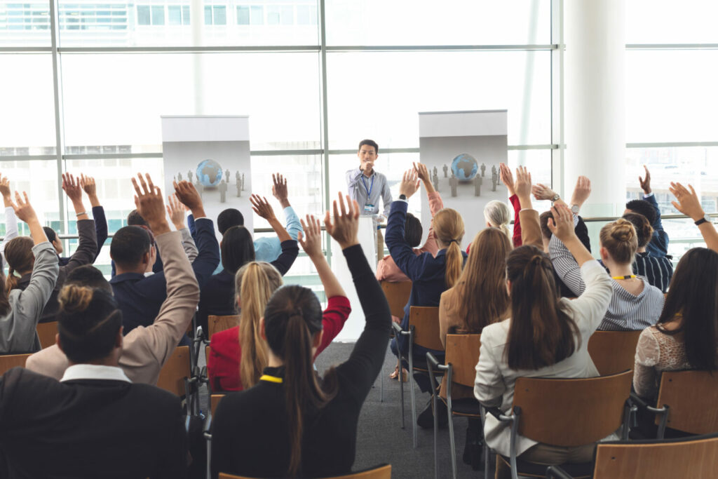 Business professionals raising hands in a business seminar Business professionals raising hands in a business seminar